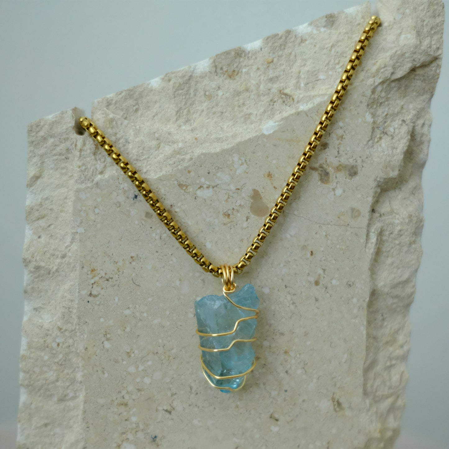 Close-up of aqua aura quartz crystal pendant wrapped in gold plating, showing shimmering blue tones and artisan detail.