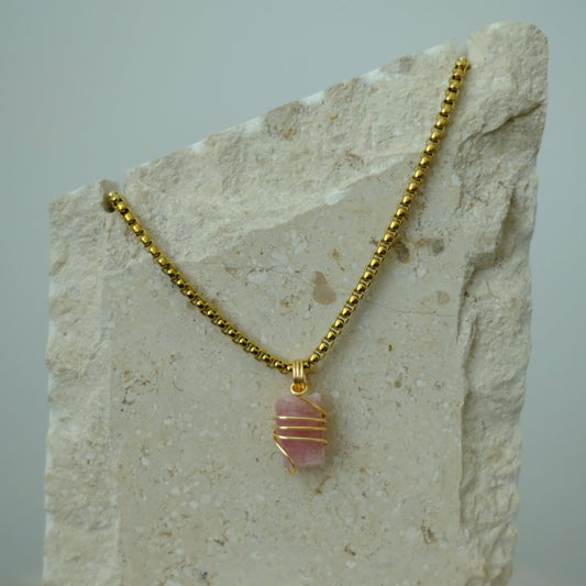 Close-up of pink tourmaline crystal wrapped in gold plating, highlighting rich pink tones and detailed artisan craftsmanship
