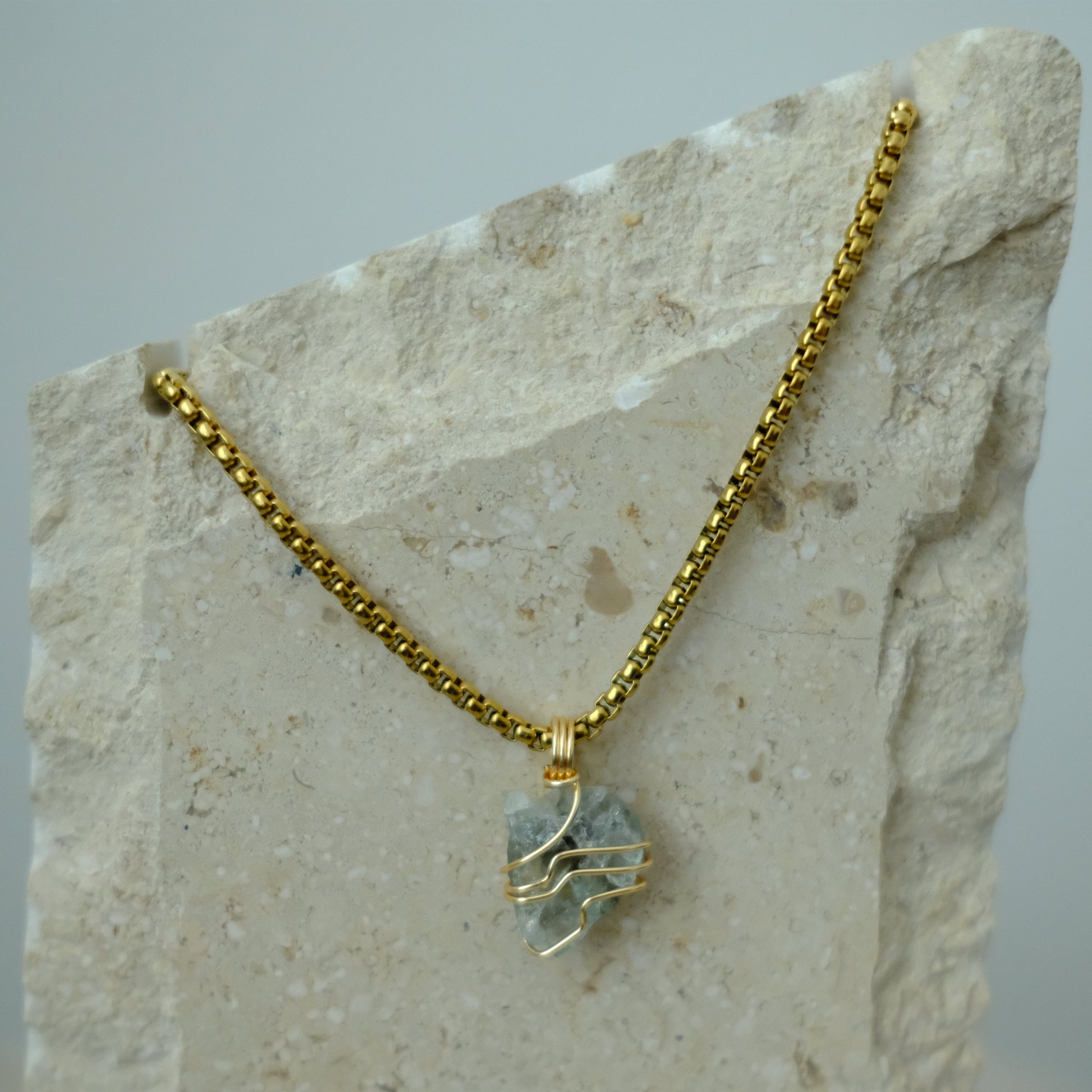 Close-up of aquamarine crystal pendant wrapped in gold plating, showing serene blue tones and artisan craftsmanship.