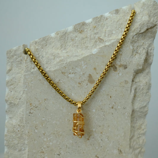 Close-up of golden topaz crystal pendant wrapped in gold plating, showcasing warm golden hues and detailed artisan craftsmanship.