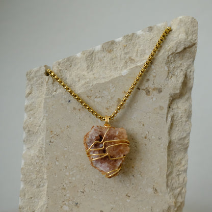 Close-up of pink amethyst crystal pendant wrapped in gold plating, showcasing soft blush tones and artisan detail.