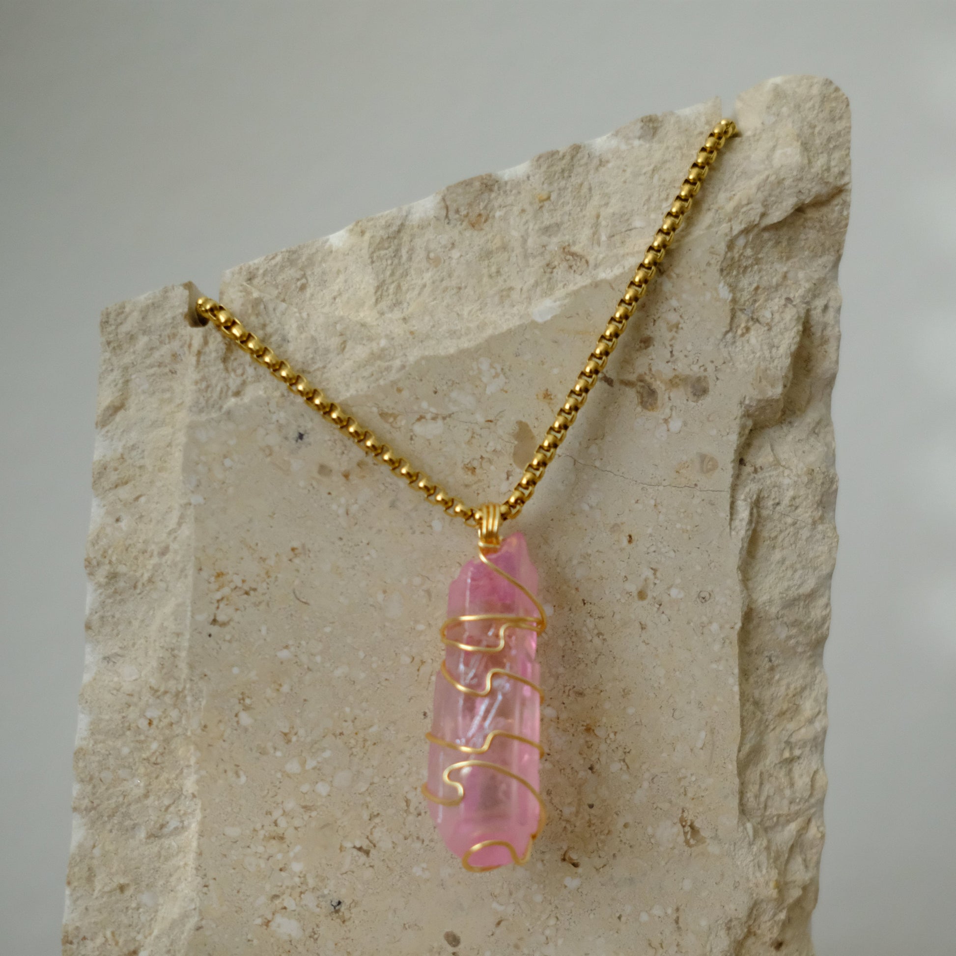 Close-up of rose aura quartz crystal wrapped in gold plating, showing shimmering pink rainbow details and artisan craftsmanship.