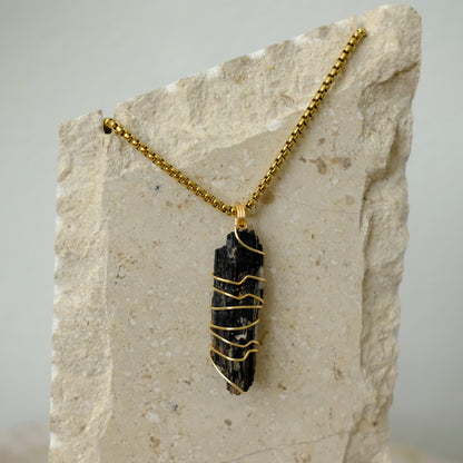 Close-up of raw black tourmaline crystal wrapped in gold plating, highlighting natural texture and luxury craftsmanship.